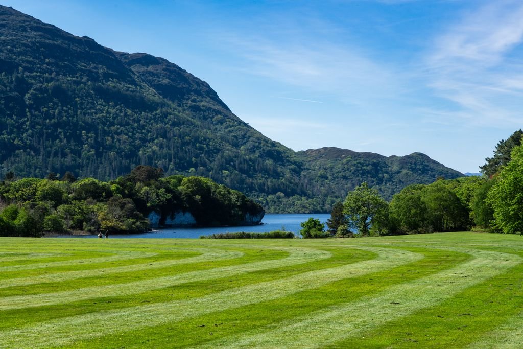 Vibrant view of lush green fields, mountains, and a lake in Ireland captured on a sunny day.